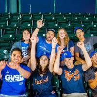 Group photo of people wearing GVSU and Tigers outfits cheering in stands at Comerica Park